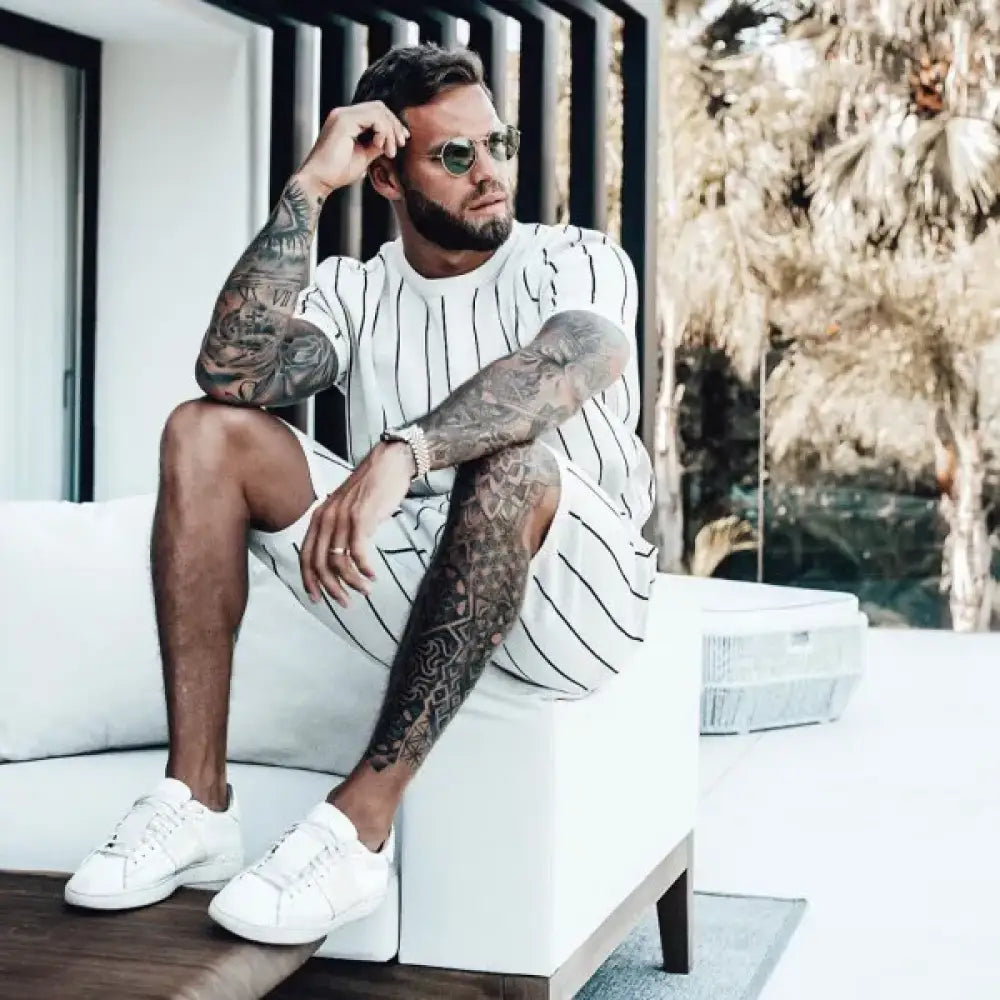 Man with tattoos sitting on a white couch in a modern indoor setting