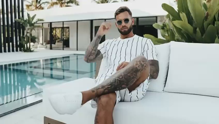 A confident man showcases a modern two-piece summer outfit in a bright, minimal setting. The camera focuses on the refined design, clean lines, and premium fabric — expressing style, comfort, and masculine elegance.